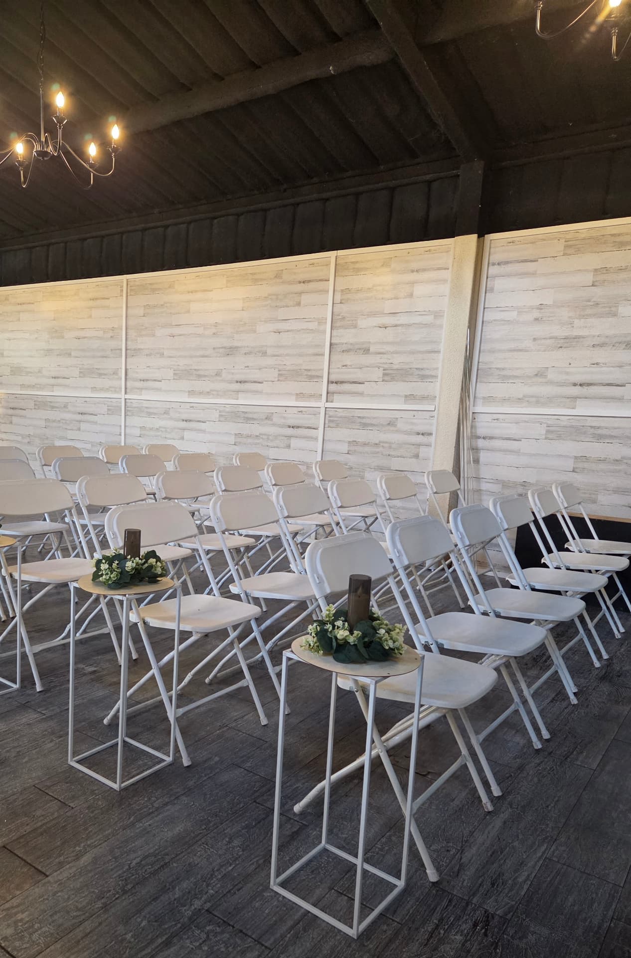 Rows of white ceremony chairs with candle and greenery pedestals